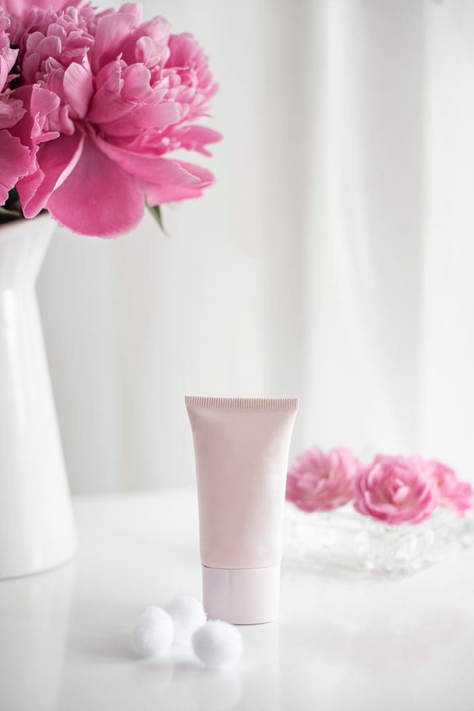 Skincare cream with pink flowers in a vase.